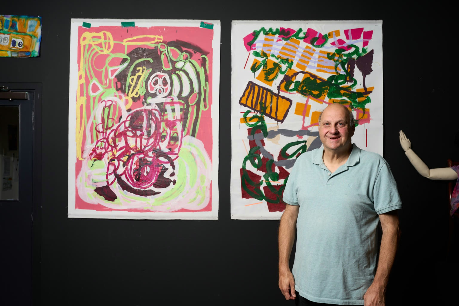 An artist standing in front of two large colourful drawings