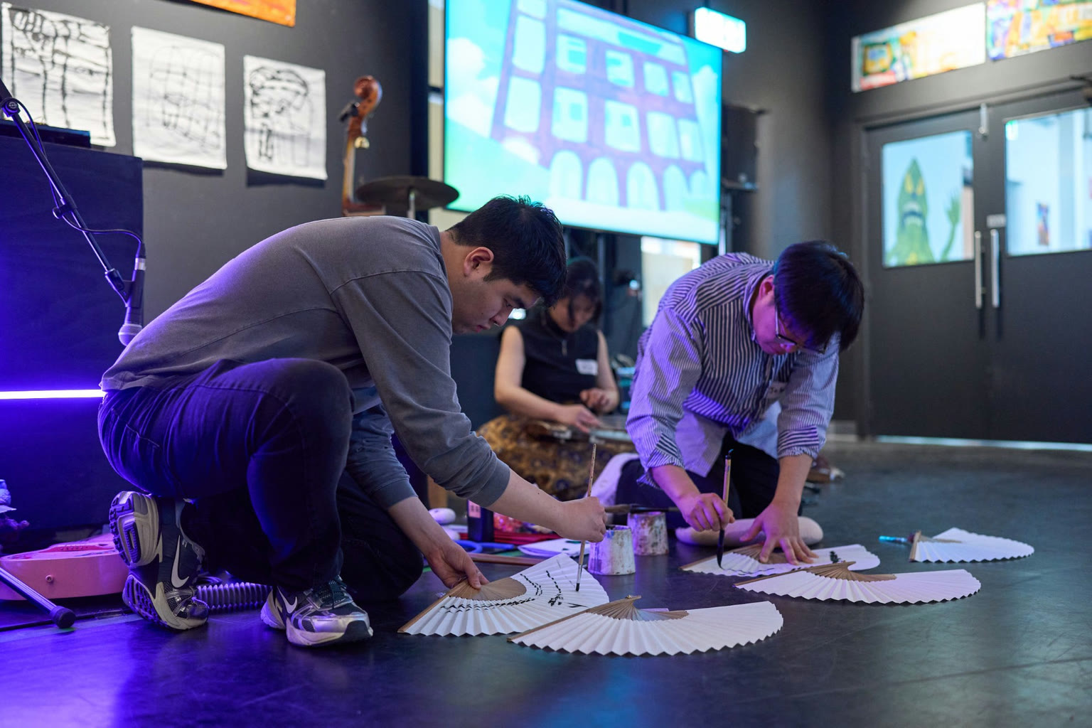 Artists painting paper fans on the floor during Deudgi
