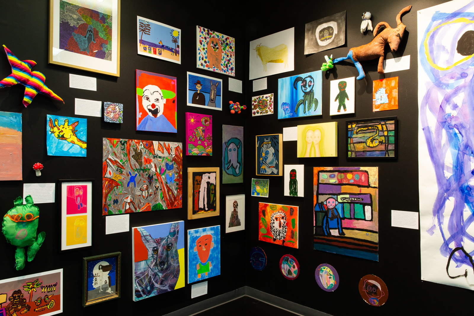 A corner of a black gallery wall densely hung with colourful works
