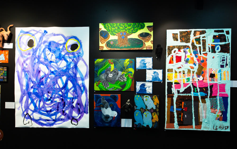Salon hang of paintings including a blue scribbled figure