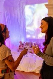 Two visitors toasting inside a pink-lit soft installation