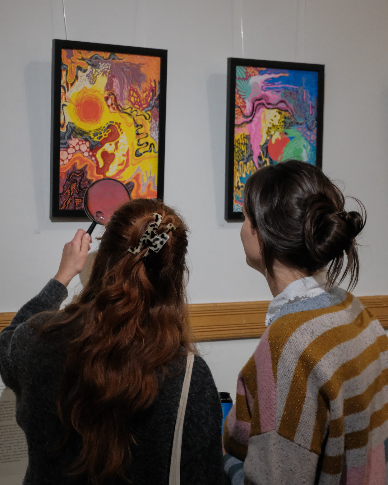 Visitors looking at two framed colourful paintings
