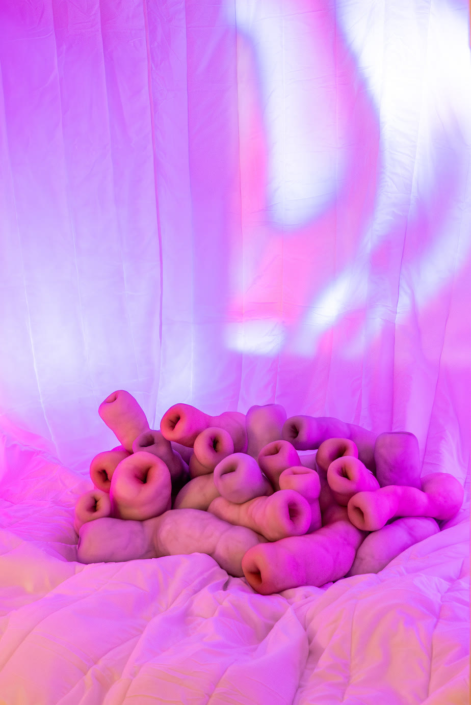 Pink sculptural forms on white fabric under violet light
