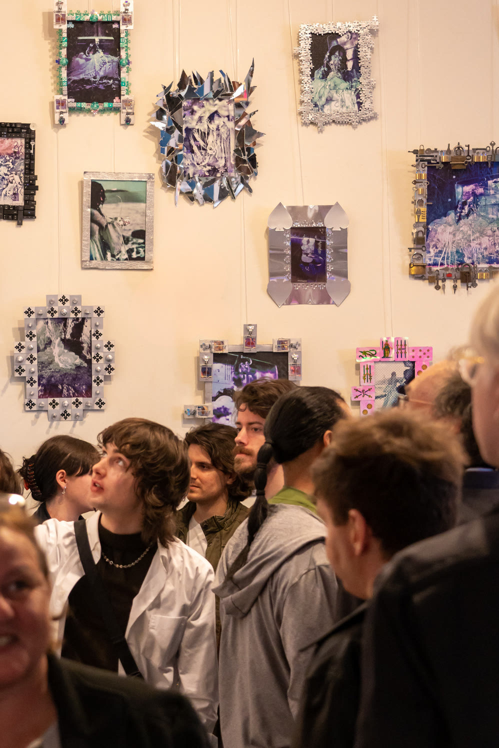 A crowd in front of a wall of framed works on opening night